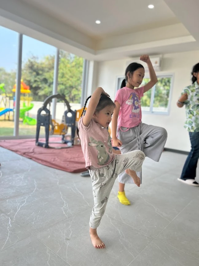 Children moving to music in a familiar SiLA classroom, with the outdoor playground visible through the window