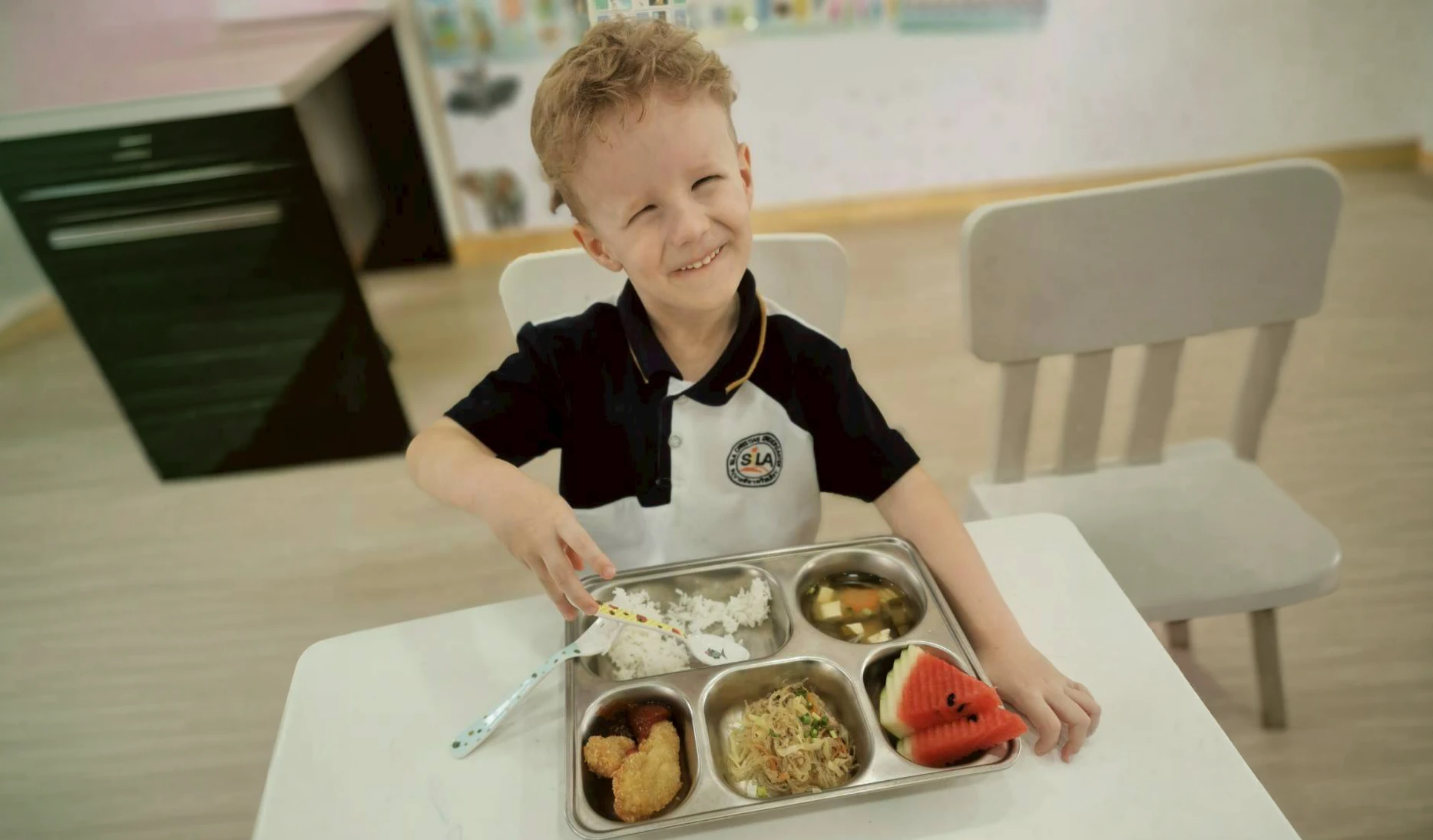A child smiling at his meal tray of rice, soup, fruit and vegetables
