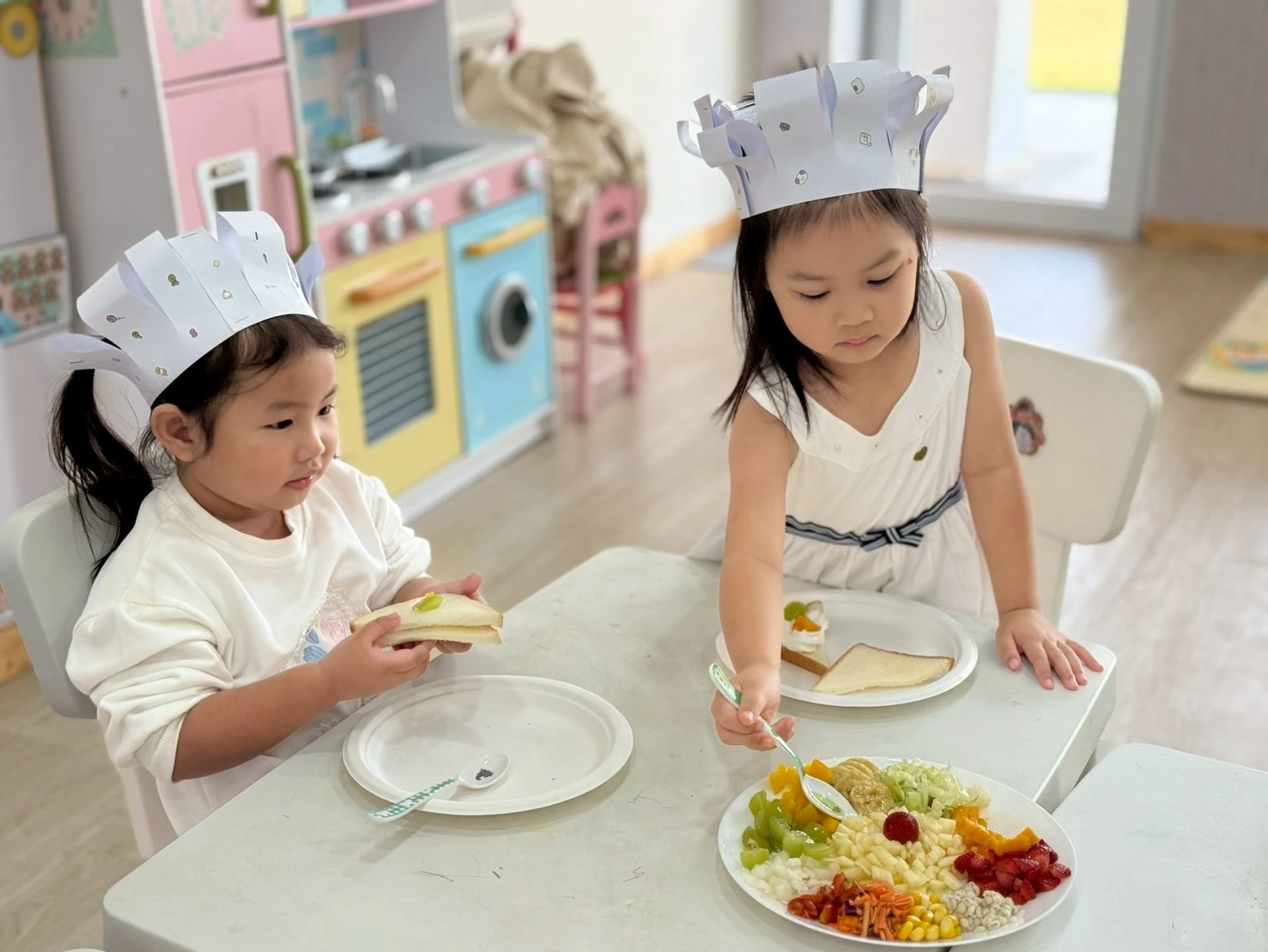 Two children in paper crowns preparing their own plates of fruit and sandwiches