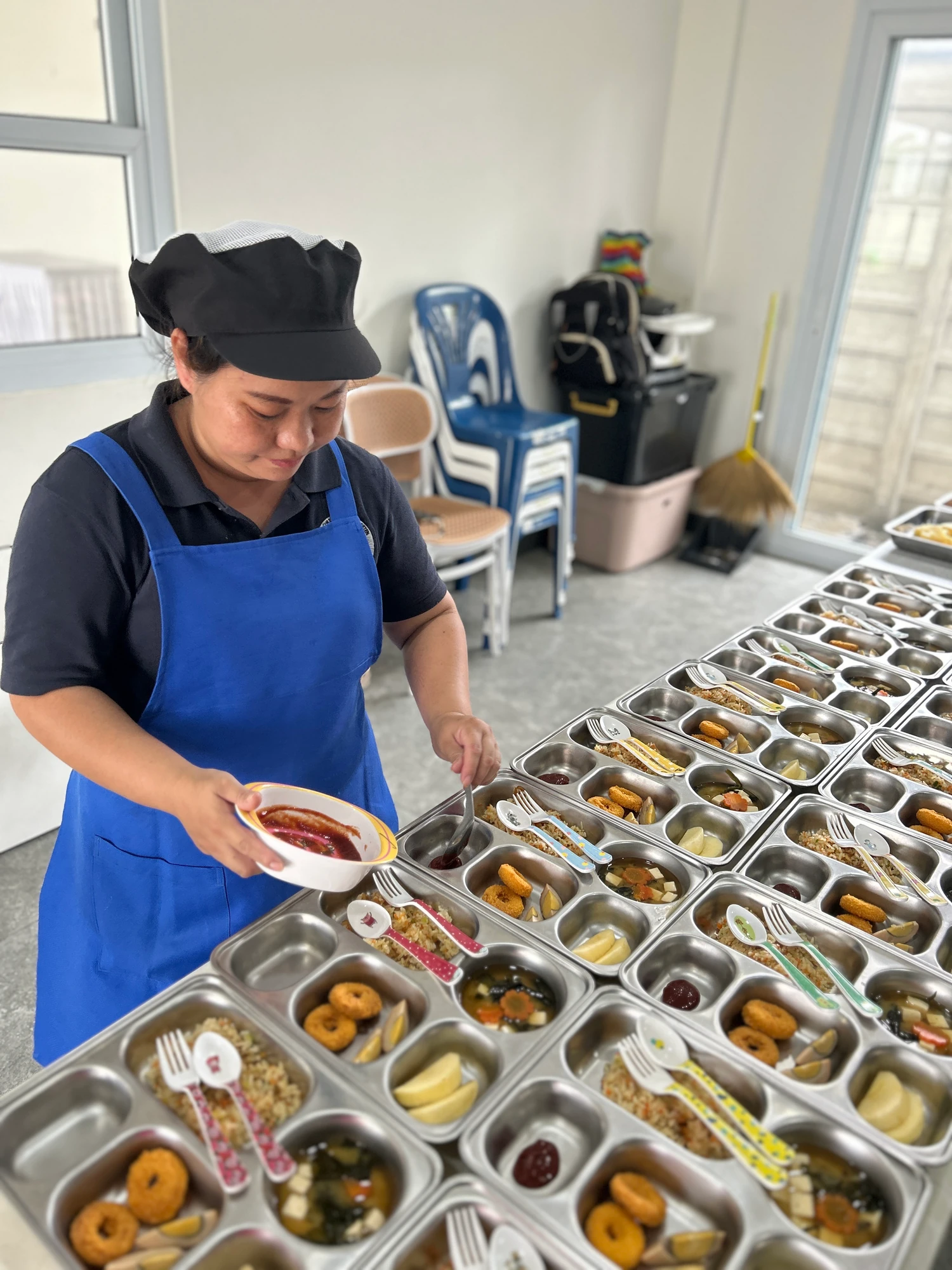 A cook plating rows of meal trays in the kitchen