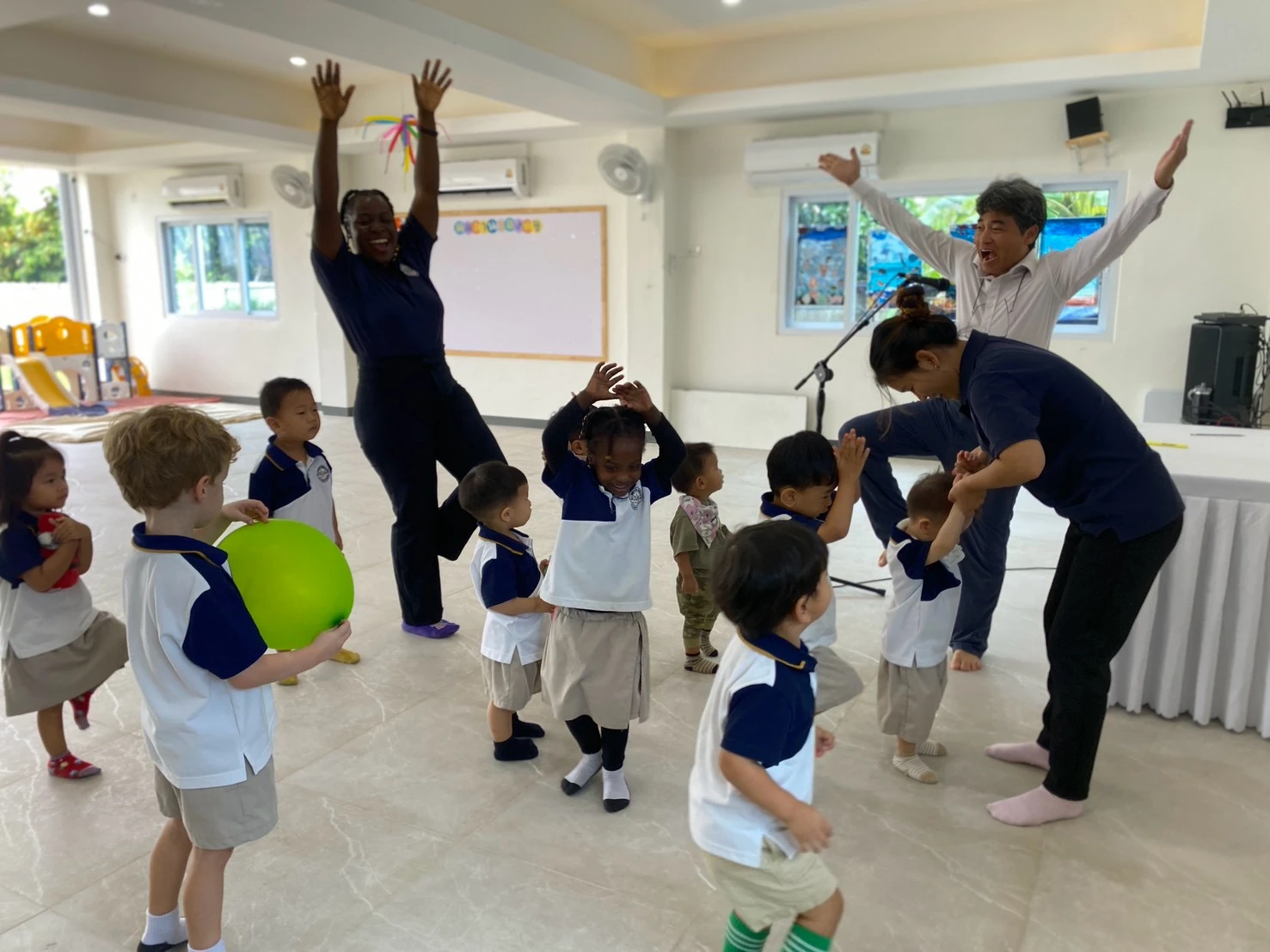 Children and teachers dancing with their arms raised during a music and movement session in the school hall