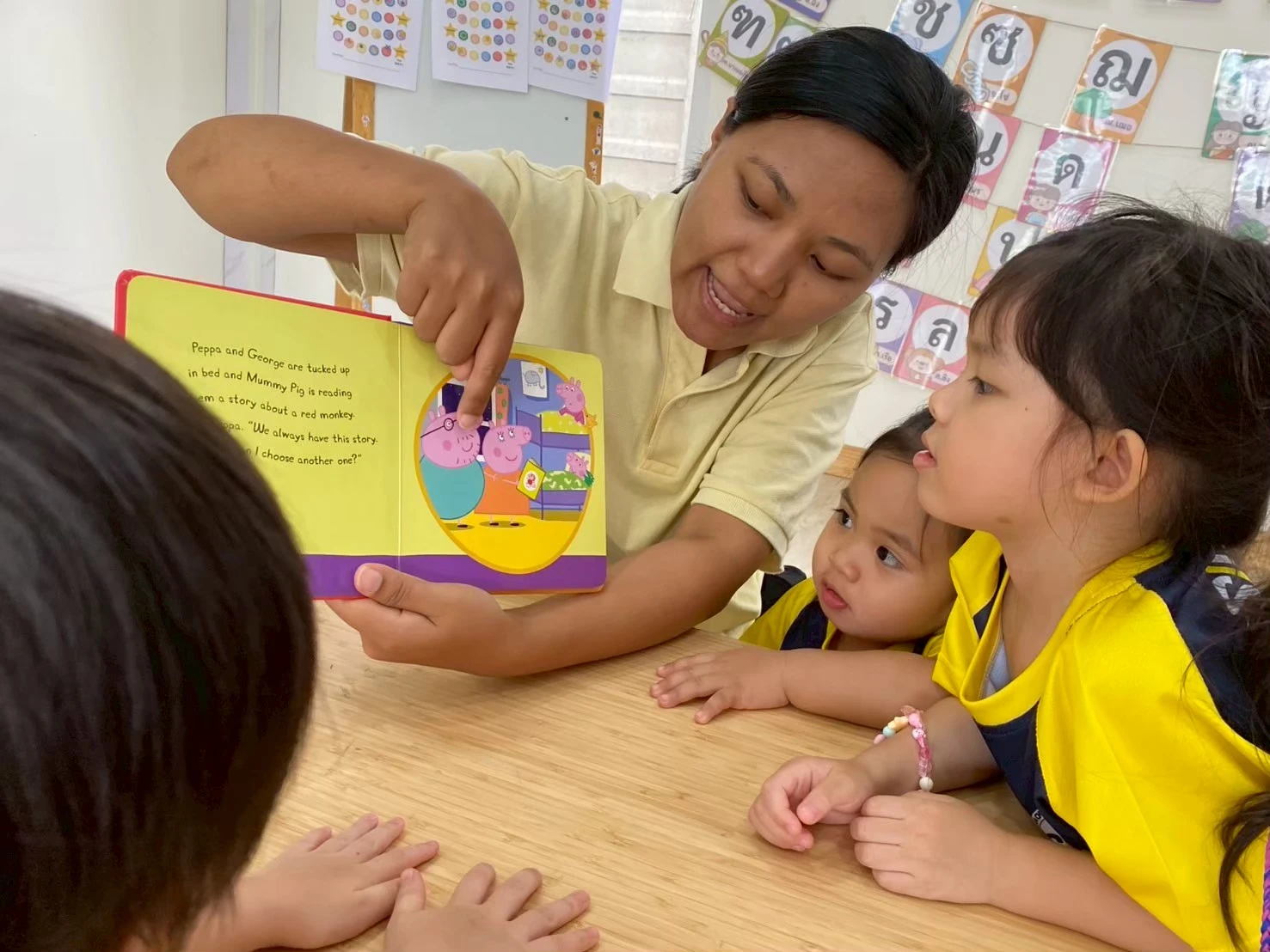 A teacher pointing at a picture book while two children look on