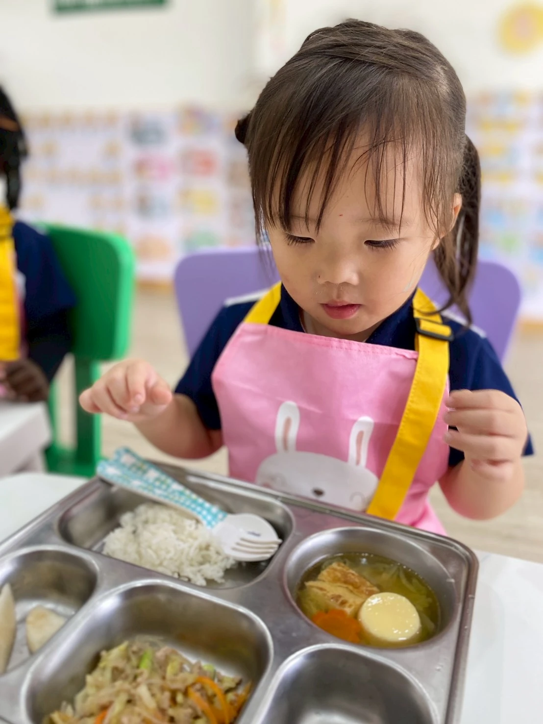 A child in a pink apron looking at her lunch tray