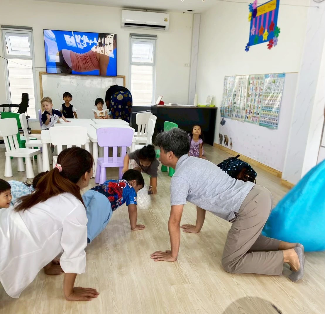 Children and adults crawling side by side along the classroom floor during a shared movement activity