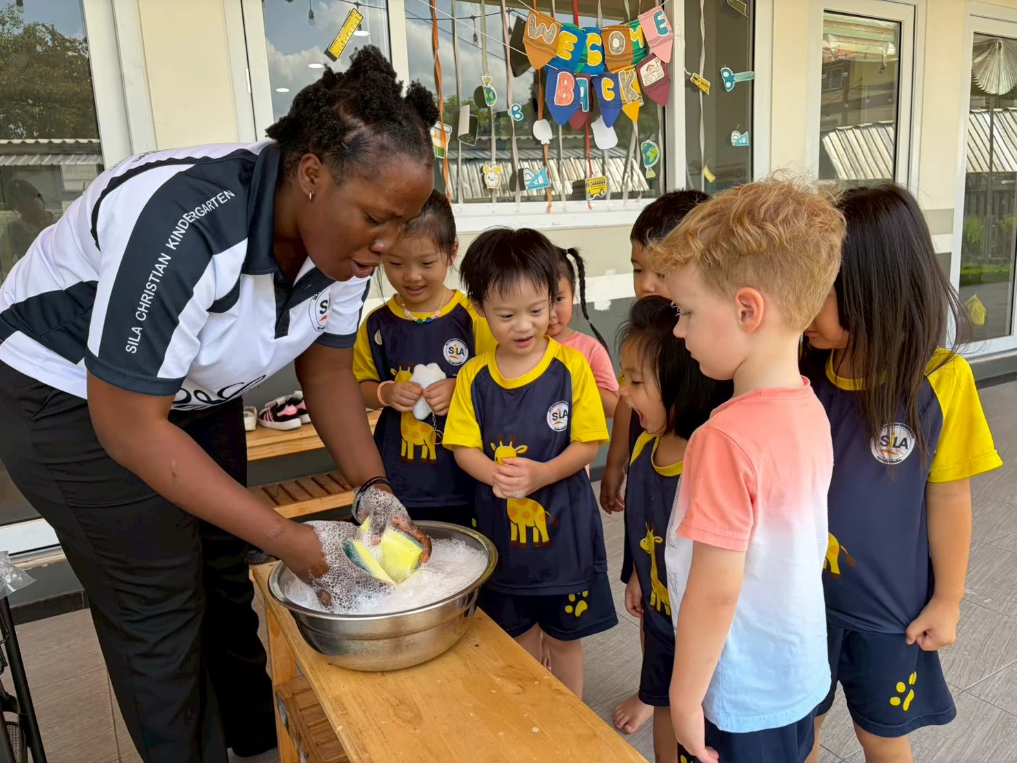 A teacher and children exploring a bowl of soap bubbles together outdoors