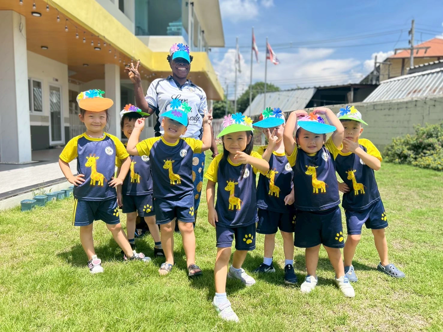 Children wearing colorful handmade sun visors outdoors on the school lawn