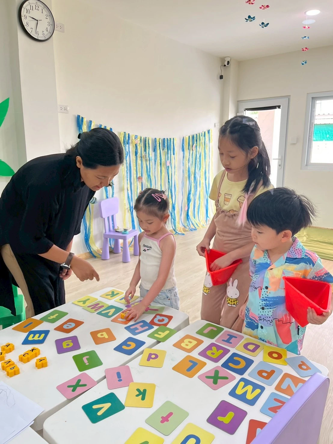 A teacher and children exploring colorful alphabet letter tiles spread across a table