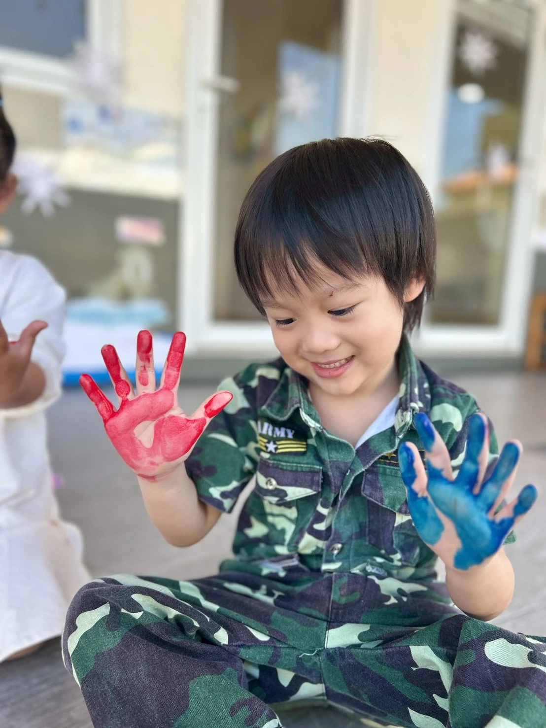 A smiling child showing off two hands freshly painted in red and blue