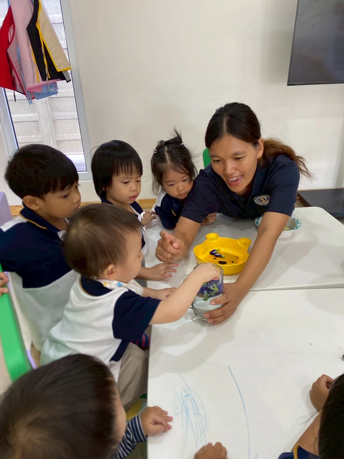 A teacher leaning down to a child's eye level during a sensory activity with flower petals and water