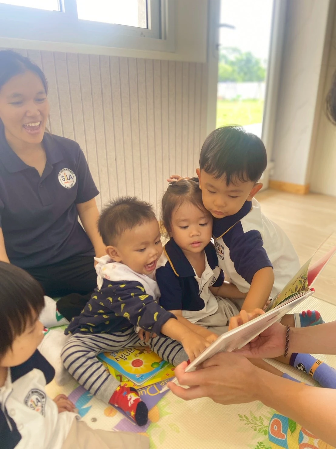 Three Nursery children leaning close together over a picture book with their teacher