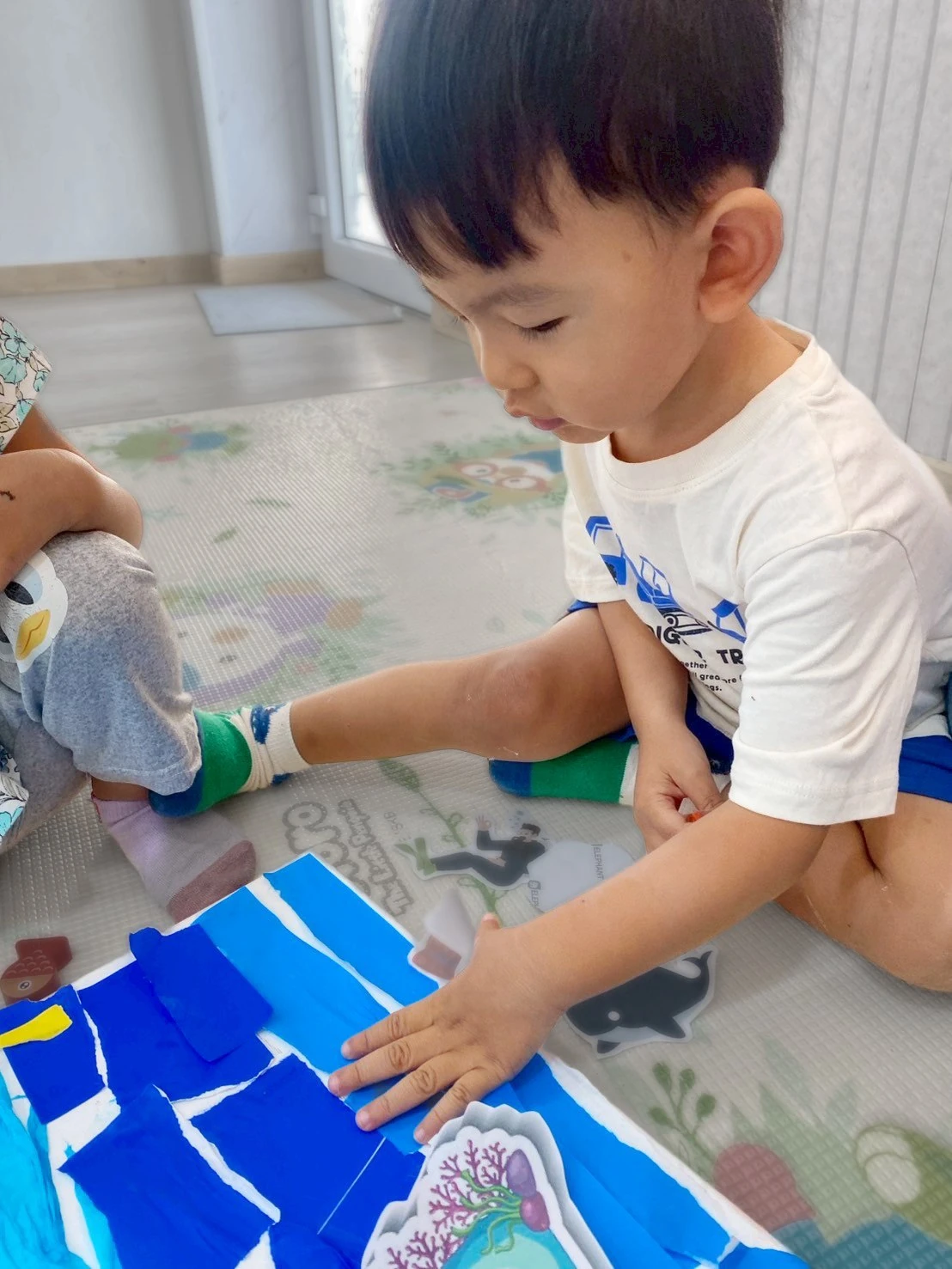 A smiling Nursery boy tilting his head playfully toward the camera outdoors
