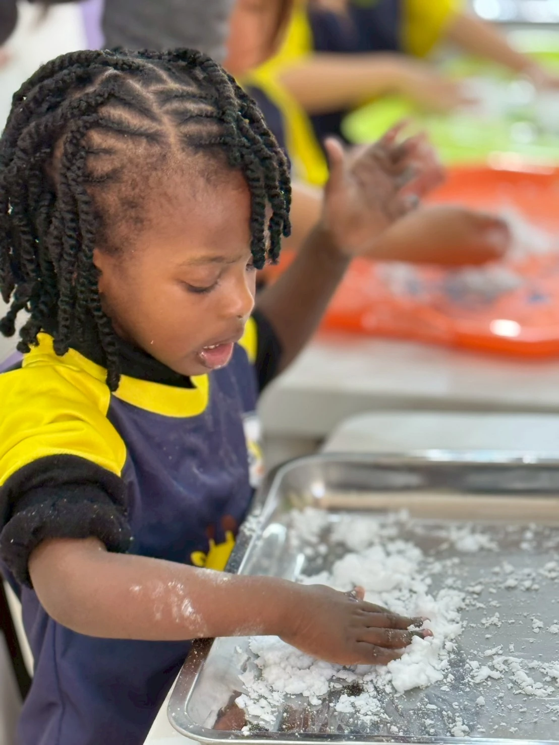 A child joyfully exploring a tray of soft sensory material with their hands