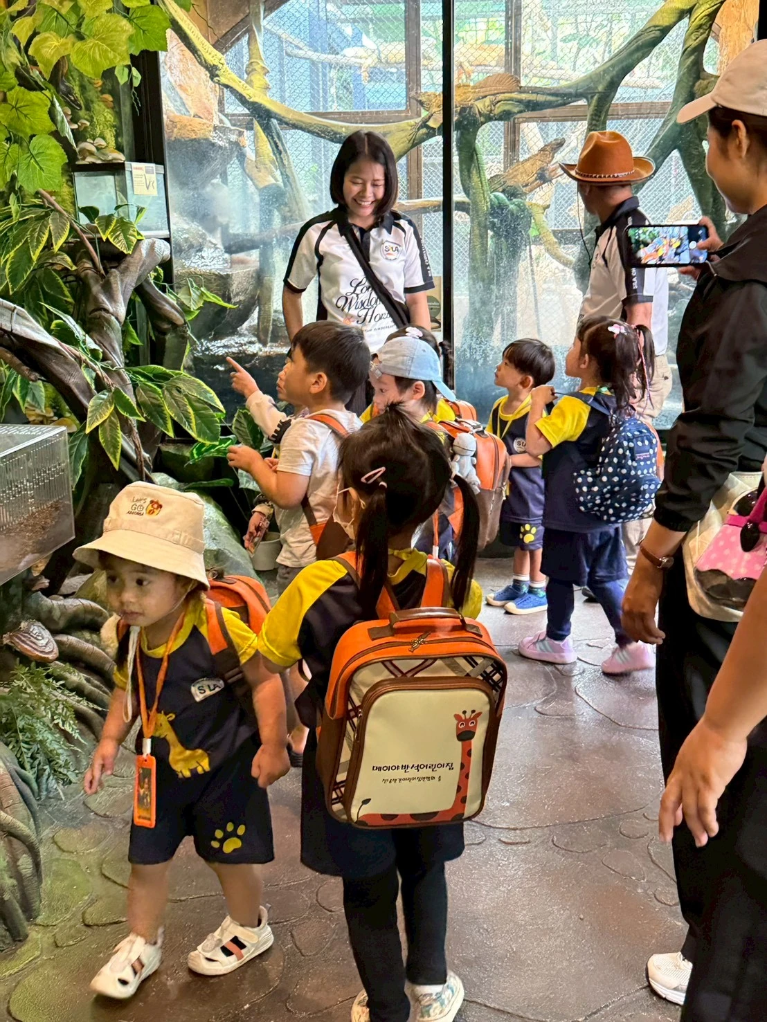 Two SiLA staff and a group of children exploring a rainforest exhibit together on a class outing